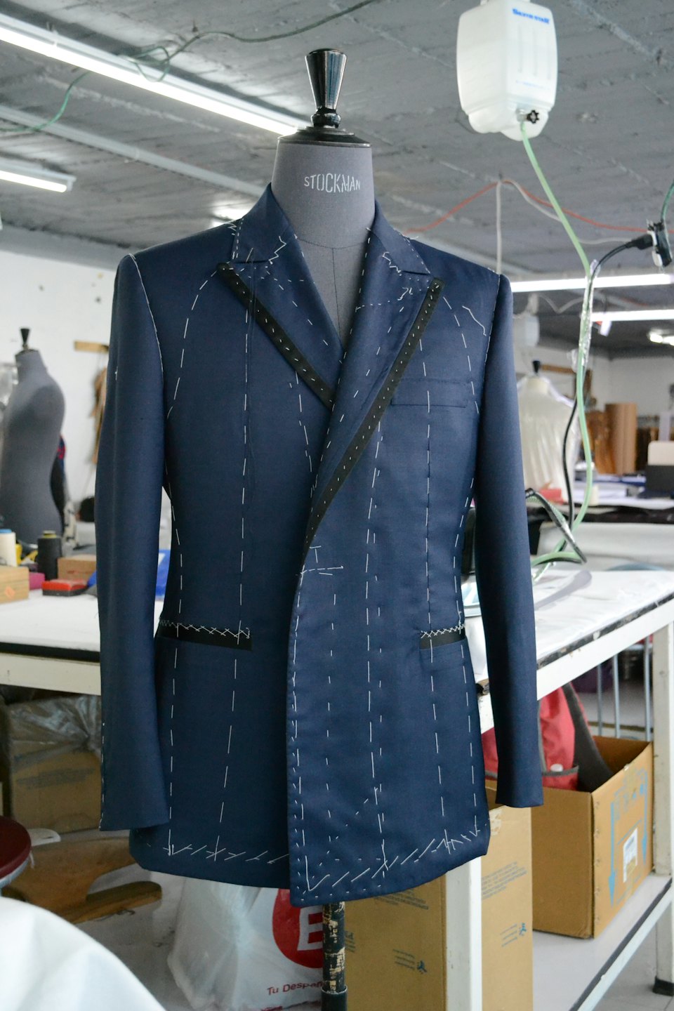 Navy blue suit jacket with white basting stitches on a mannequin.